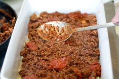 a spoon is being used to scoop food out of a casserole dish with meat sauce