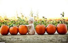 a baby sitting on the ground surrounded by pumpkins