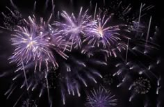 fireworks are lit up in the night sky with purple and white lights on it's sides