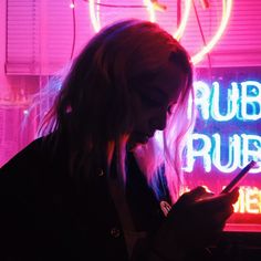 a woman using her cell phone in front of a neon sign