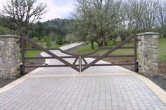 a gated driveway leading to a grassy area with trees in the background and stone pillars on either side