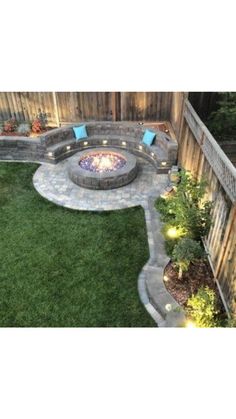 an outdoor fire pit surrounded by green grass and landscaping lighting up the area around it