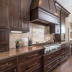 a large kitchen with wooden cabinets and stainless steel stove top oven in the center, surrounded by wood flooring