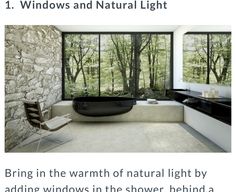 a modern bathroom with stone walls and large windows overlooking the trees outside, along with a black bathtub