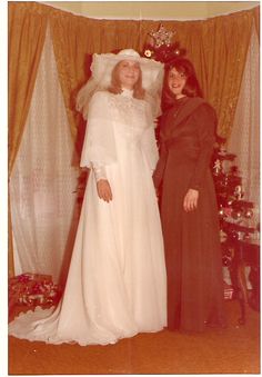 two women in wedding dresses standing next to each other near a christmas tree with presents on it