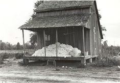 an old black and white photo of a barn with hay piled on the front porch