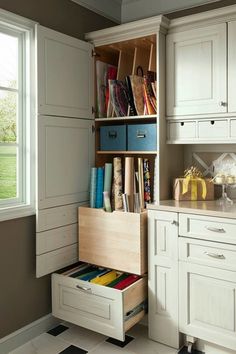 a kitchen with white cupboards and drawers filled with books, magazines and other items