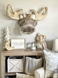 a wooden table topped with pillows and stuffed animals next to a wall mounted deer head