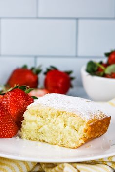 a piece of cake with powdered sugar on top and strawberries in the background