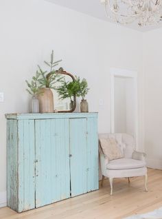 a room with a chair, mirror and plant on top of the cabinet in it