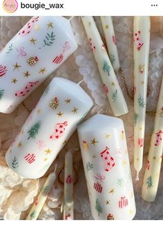 four white candles with christmas designs on them sitting next to lace doily and paper