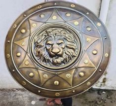 a man holding a large metal shield with a lion face on it's side