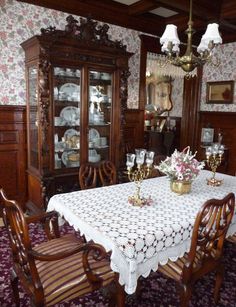 a dining room table with chairs and china cabinet in the backround, surrounded by floral wallpaper