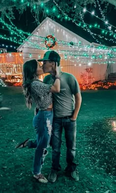 a man and woman kissing in front of a house with christmas lights on the roof