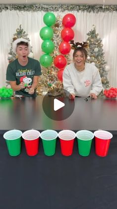 two people sitting at a table with cups in front of them and balloons on the wall behind them