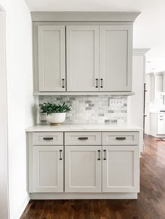 a white kitchen with wooden floors and cabinets in it's center island, along with a potted plant on the counter