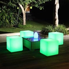 three glowing cube chairs and a table on a deck at night with trees in the background