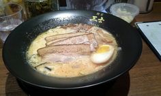 a black bowl filled with meat and eggs on top of a wooden table next to water