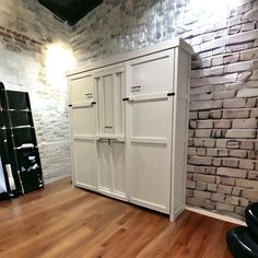 a white cabinet sitting on top of a hard wood floor next to a brick wall