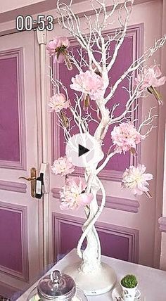 a white vase with pink flowers on top of a table in front of a door