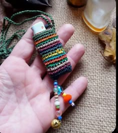 a hand holding a small cell phone case made out of beads and other things on the table