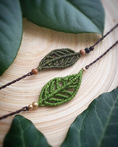 two necklaces with green leaves and beaded beads on a wooden surface next to large leaf