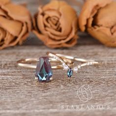 two gold rings with blue topazte and pearls on wooden table next to roses