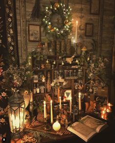 a table topped with lots of candles next to a wall covered in pictures and wreaths