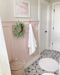 a bathroom with pink walls and black and white flooring, wreath on the wall