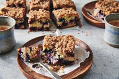 blueberry crumb bars on a wooden plate next to two cups of tea