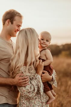 a man and woman holding a baby in their arms while standing in an open field