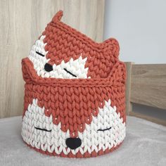 an orange and white knitted bag with a fox face on the front, sitting on top of a bed