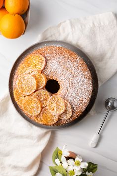 an orange cake with powdered sugar on top next to some oranges and flowers