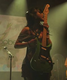 a woman singing into a microphone while holding an electric guitar