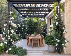 an outdoor dining area with table and chairs surrounded by white flowers on the side walk