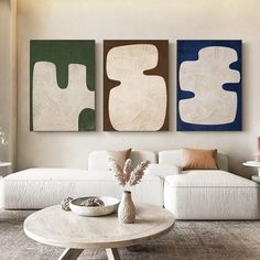 three abstract paintings hang on the wall above a coffee table in a modern living room