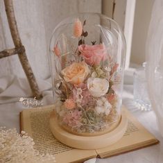 there is a glass dome with flowers in it on top of a book and other items