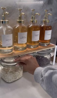 a shelf with soaps and lotion bottles on top of it, in front of a woman's hand