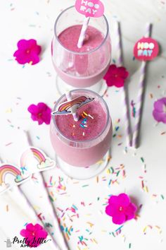 two glasses filled with pink smoothie on top of a table next to sprinkles