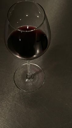 a glass of red wine sitting on top of a metal table next to a cell phone