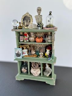 a green shelf filled with lots of different items on top of a black table next to a white wall