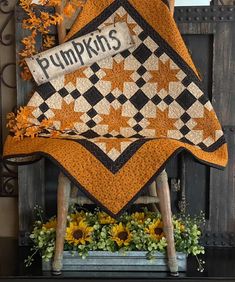 a quilted pumpkin sitting on top of a wooden chair next to sunflowers