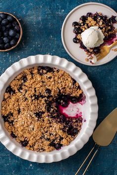 a blueberry crumble pie with ice cream on top and two bowls of berries in the background