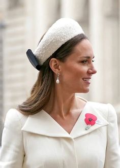 a woman wearing a white coat with a red flower on it's lapel