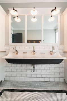 a black and white bathroom sink under two mirrors with three lights on the wall above it