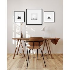 three framed pictures hang on the wall above a wooden desk with a chair and lamp