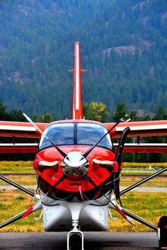 an airplane parked on the tarmac with mountains in the backgrouund and trees in the background