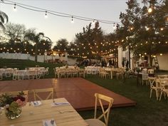 tables and chairs are set up on the lawn for an outdoor dinner or party with string lights strung above them