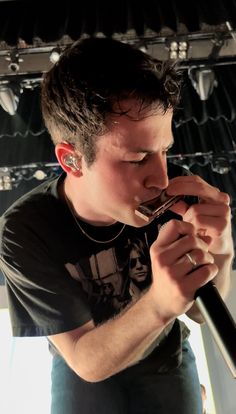 a young man holding a microphone in his hand and looking down at the ground while wearing a black t - shirt