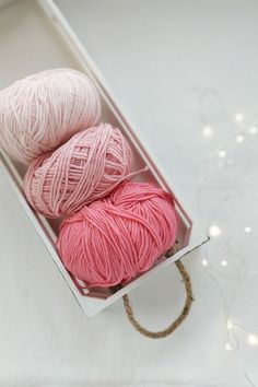 three balls of yarn in a box on a white tablecloth with string lights behind them